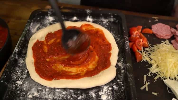 Per fare una pizza classica, ungere l'impasto con la salsa