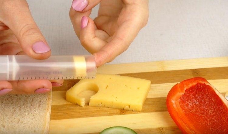 Drücken Sie mit einer Spritze einen Kreis aus einer Käsescheibe.